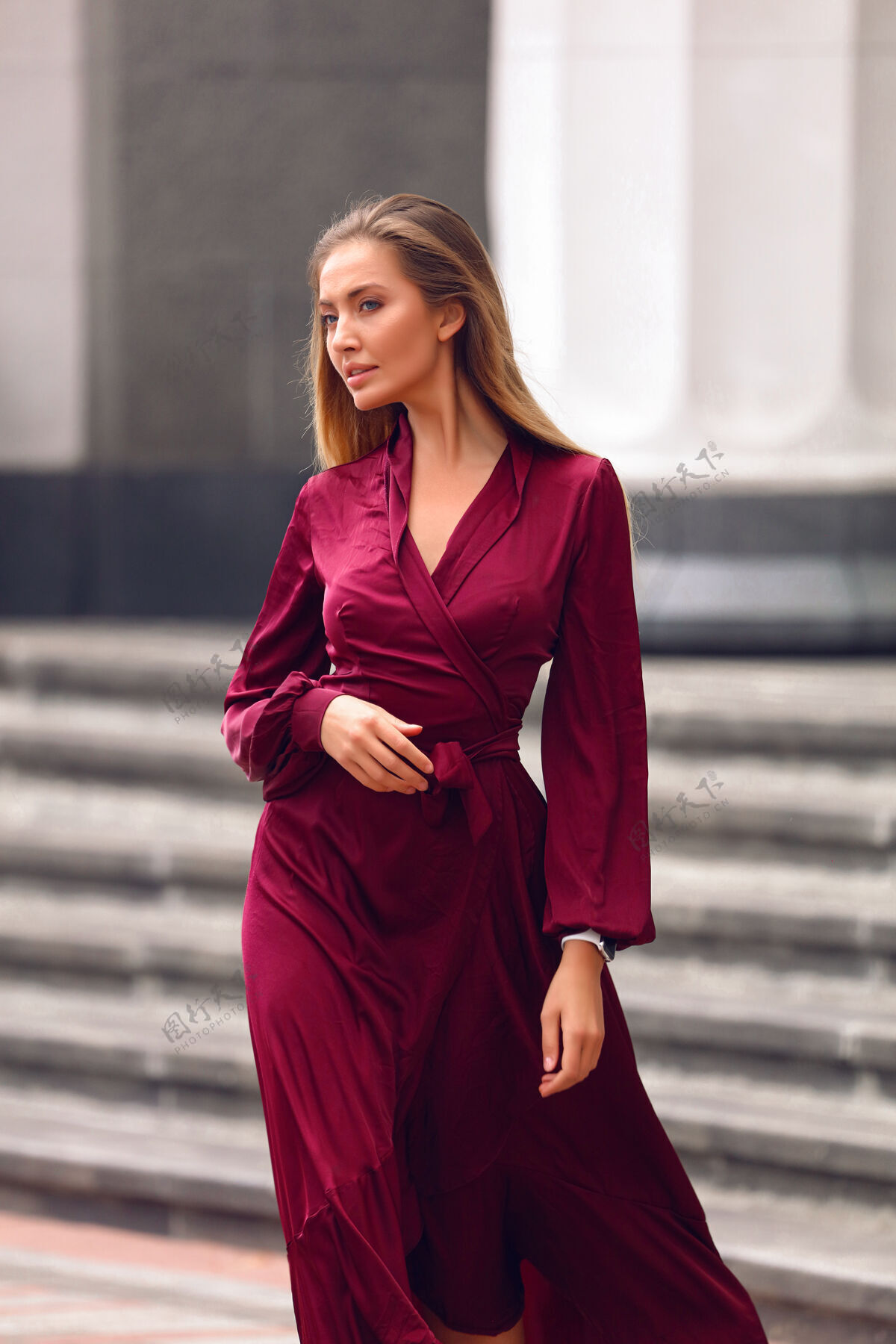 淑女优雅的年轻女士 身着紫红色长裙 袖子和腰带手放在胸前金发 自然的裸妆走在大楼附近的街道上经典温柔发型