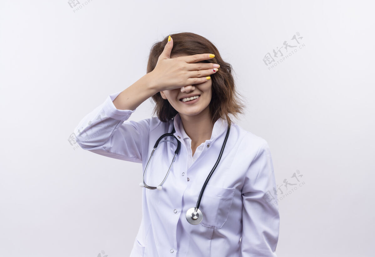 听诊器身穿白大褂的年轻女医生戴着听诊器捂着眼睛 手上露出愉快的笑容女人站着手