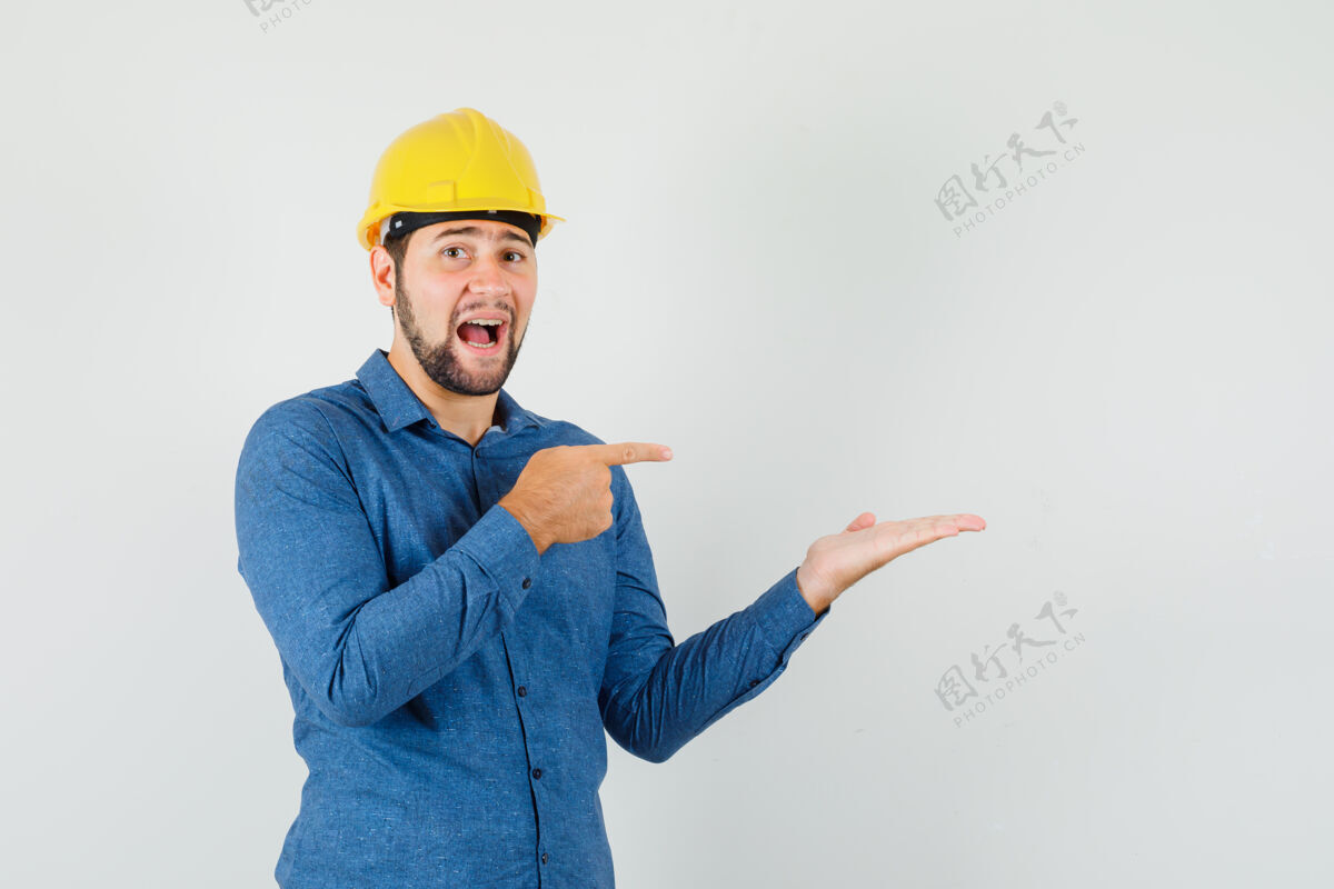 成功年轻的工人指着他摊开的手掌 穿着衬衫 戴着头盔 看上去很兴奋专业库存计算机