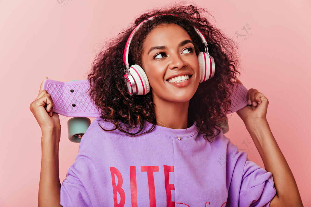 成人穿着紫色衬衫的正面女模特微笑着抬头看的特写镜头可爱的非洲年轻女士戴着耳机听着最喜欢的歌模特年轻舞蹈