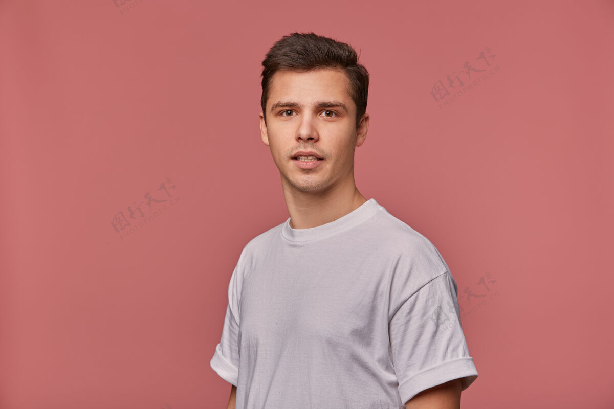 计划一个穿着白t恤的年轻人的画像 带着质疑的表情 站在粉红色的墙上沉思模特男人