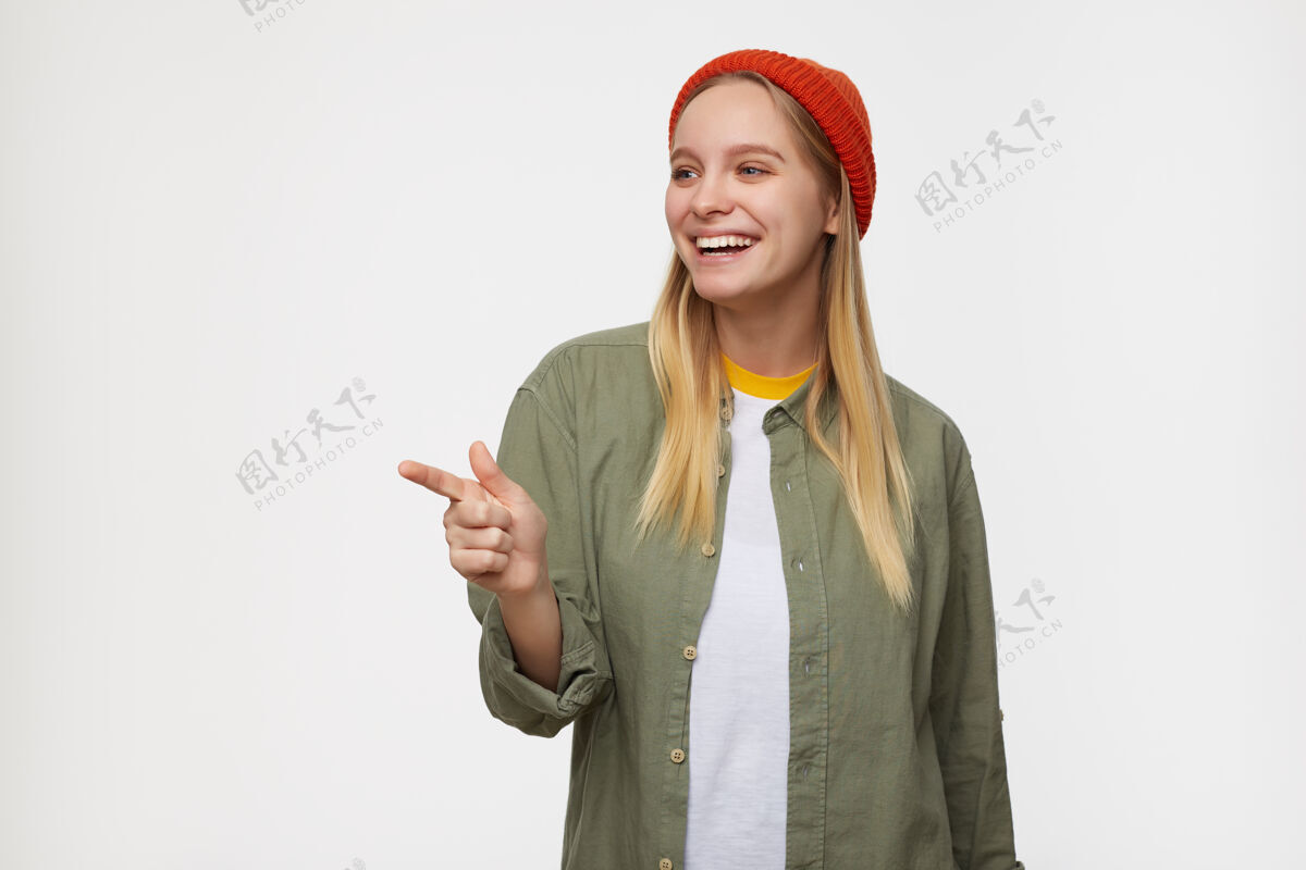 女性室内写真：年轻可爱的金发碧眼的金发女郎一边用食指指着一边欢笑 一边穿着休闲服站在蓝色的衬托下提高快乐积极