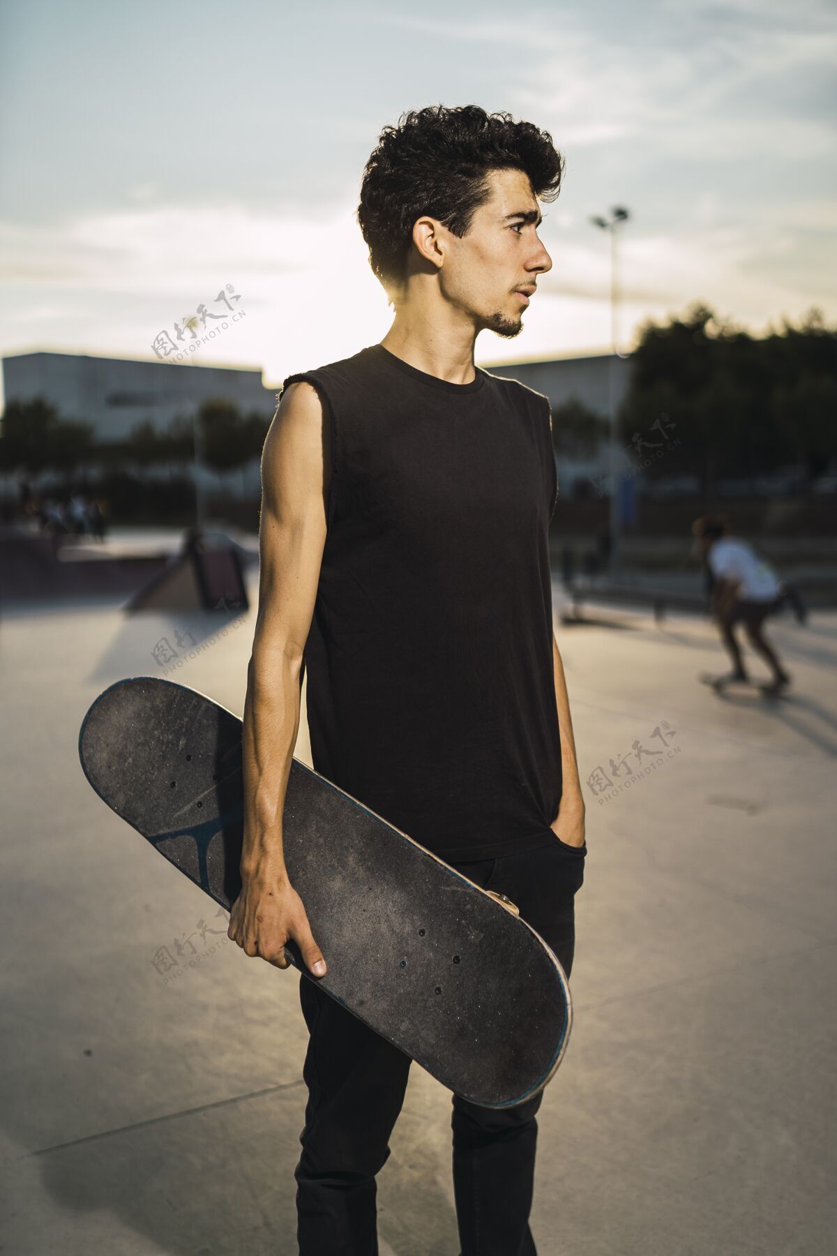 街道一个年轻的运动男 穿着黑色衣服 手插在口袋里 手里拿着一块滑板垂直滑板年轻