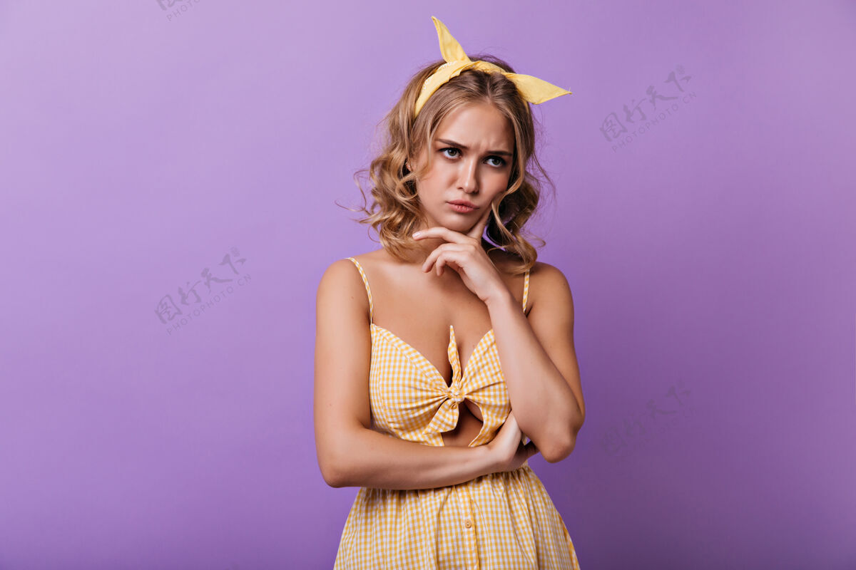 悲伤戴着黄丝带的悲伤的年轻女子在紫色的头发上摆着姿势穿着夏装的沉思的卷发女士的室内肖像服饰快乐金发