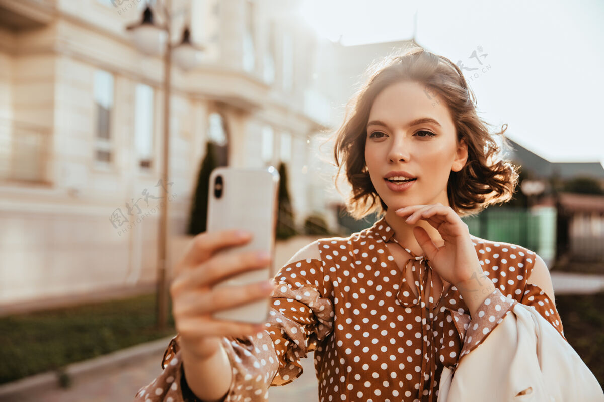寒冷漂亮优雅的女人拿着智能手机自拍穿着棕色裙子的欧洲女人在街上摆姿势人可爱休闲