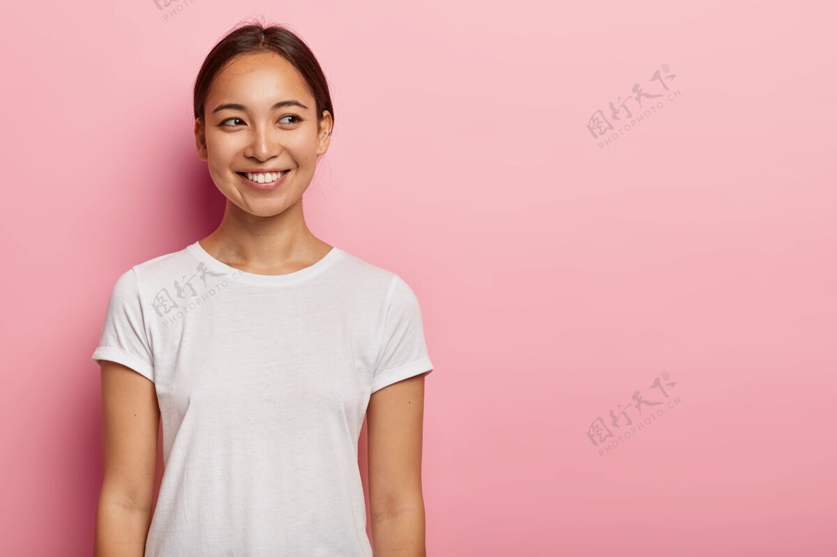 亚洲人快乐亚洲女青年镜头有温柔的微笑 表情妩媚的侧视 穿着休闲的白色t恤 有自然的美 隔离在粉色的墙上人与情感的概念人积极黑发