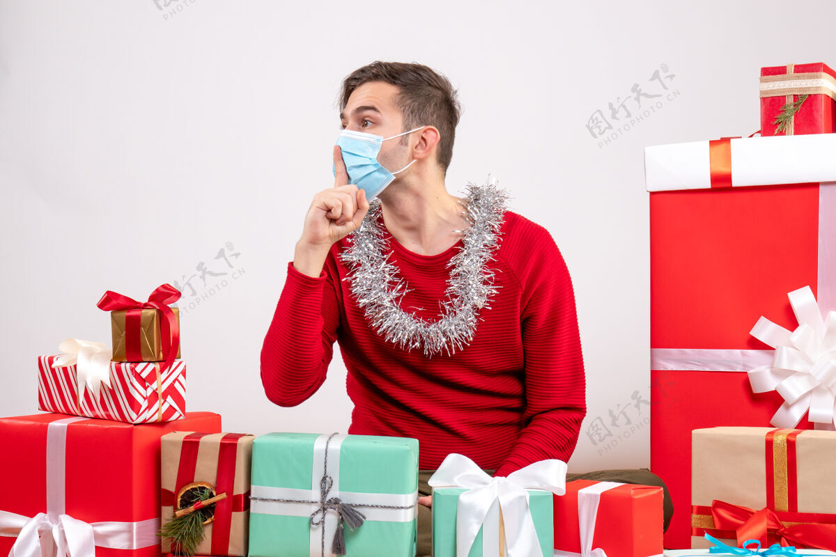 年轻人正面图：戴着面具的年轻人打着嘘的手势 围坐在圣诞礼物旁边人嘘礼物