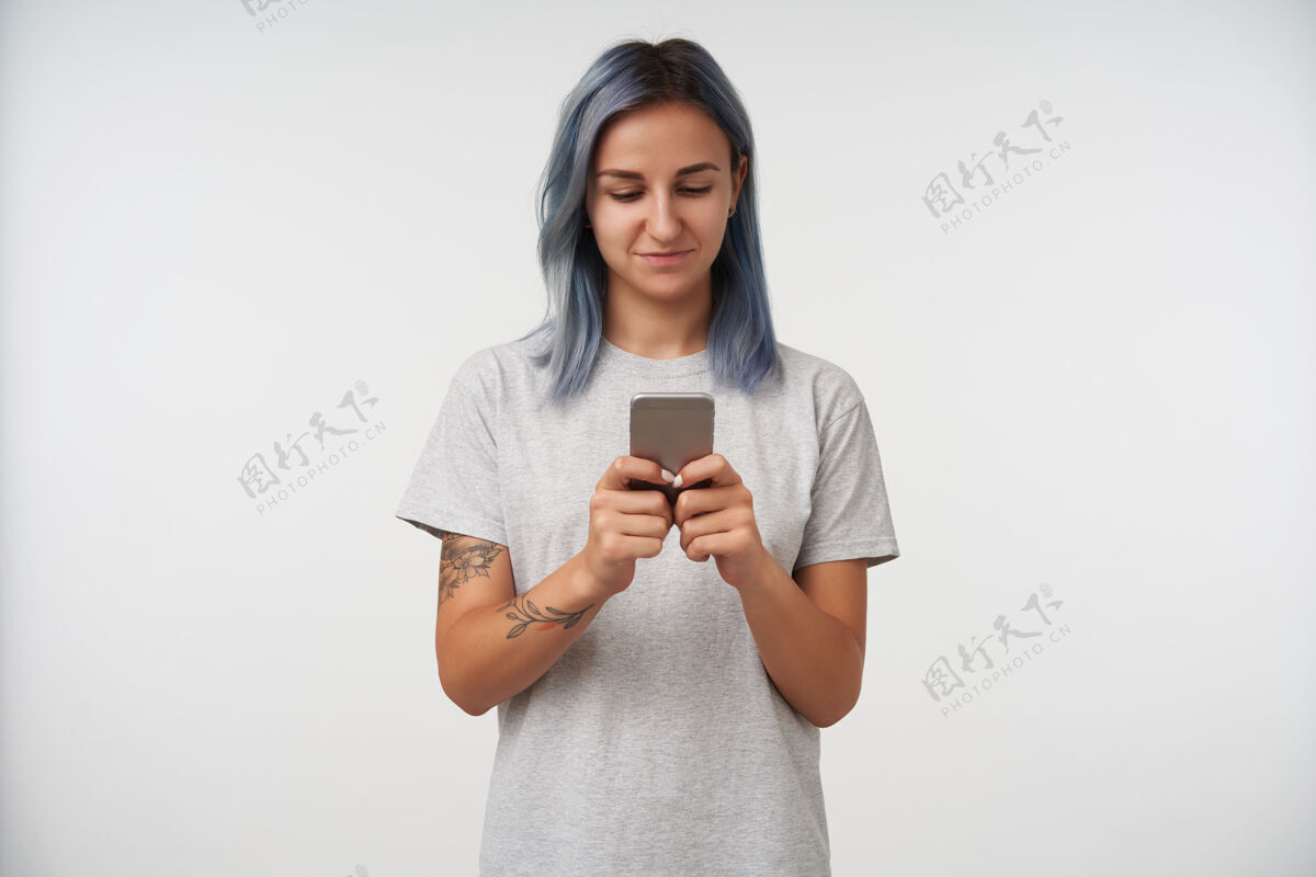灰色积极的年轻漂亮的蓝发女纹身保持手机在举起的手 同时检查她的信息 隔离在白色室内衣服肖像