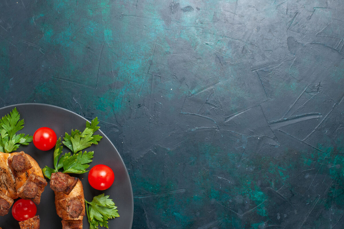 盘子顶视图切碎的熟肉和绿色樱桃番茄在深蓝色背景的盘子里健康水果樱桃番茄
