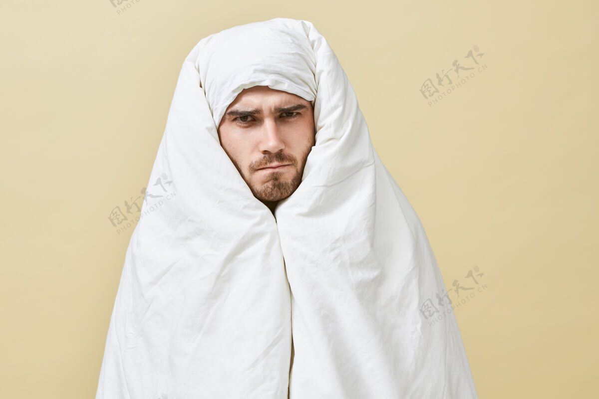 毯子这是一个孤独的镜头 拍摄的是一个沮丧困倦的年轻男性 他愤怒而不快的面部表情皱眉 不愿意去上班 宁愿呆在温暖的床上 裹着白毯子格子抑郁肖像