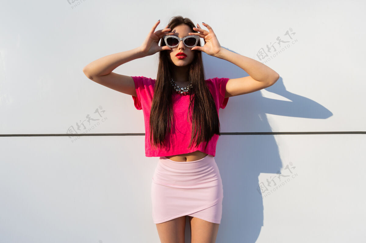 女孩穿着夏装 戴着太阳镜的时尚黑发女人在白色的城市墙上摆姿势街道成人墙