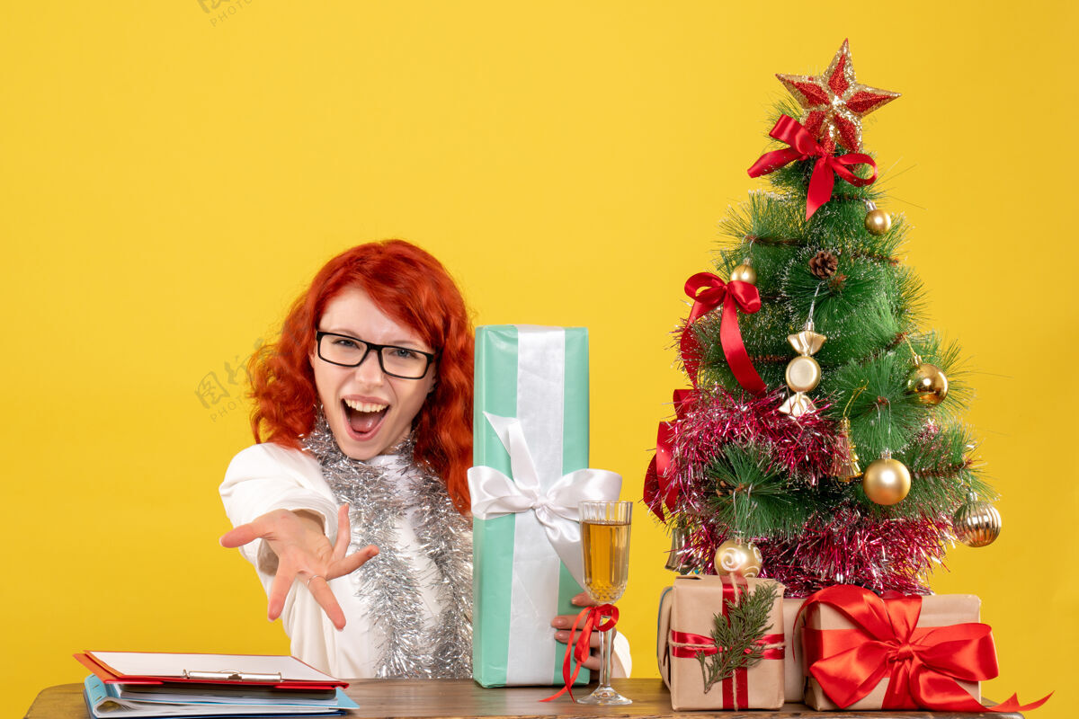 安排前视图：女医生拿着圣诞礼物和黄色背景上的圣诞树坐着快乐花礼物