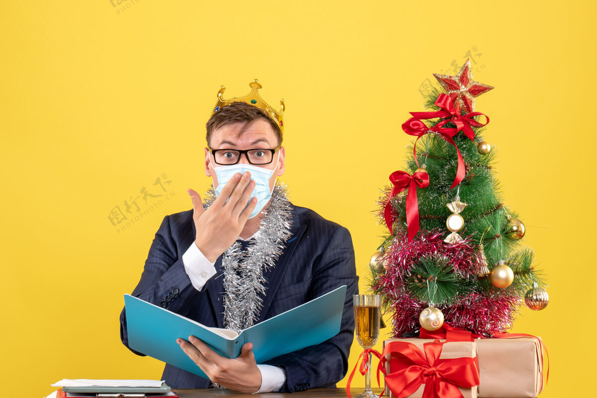 商务前视图的商人与皇冠举行文件档案坐在桌旁圣诞树和黄色的礼物成人表演者圣诞节