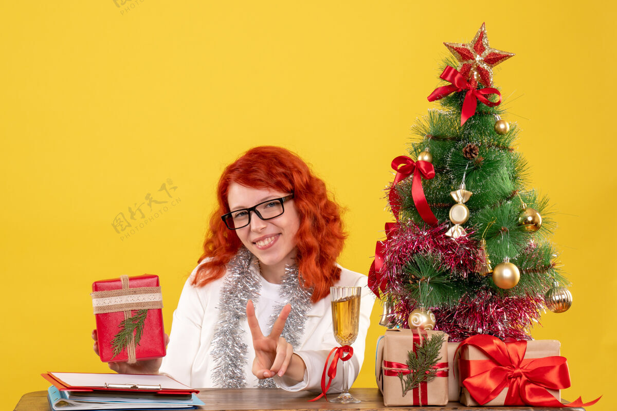插花前视图：女医生坐在桌子后面 黄色背景上有圣诞礼物快乐肖像情感