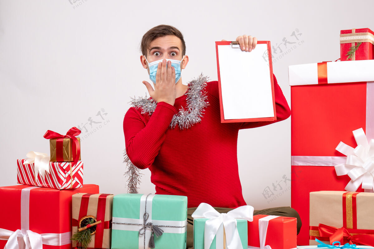 坐着正面图：戴着面具拿着剪贴板的年轻人围坐在圣诞礼物旁礼物盒子圣诞节