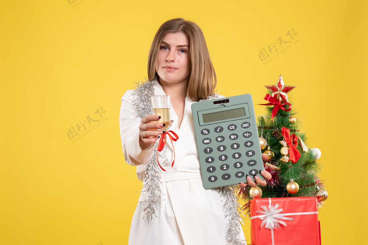 微笑正面图女医生站着拿着计算器 背景是黄色的圣诞树和礼品盒抱着肖像女医生