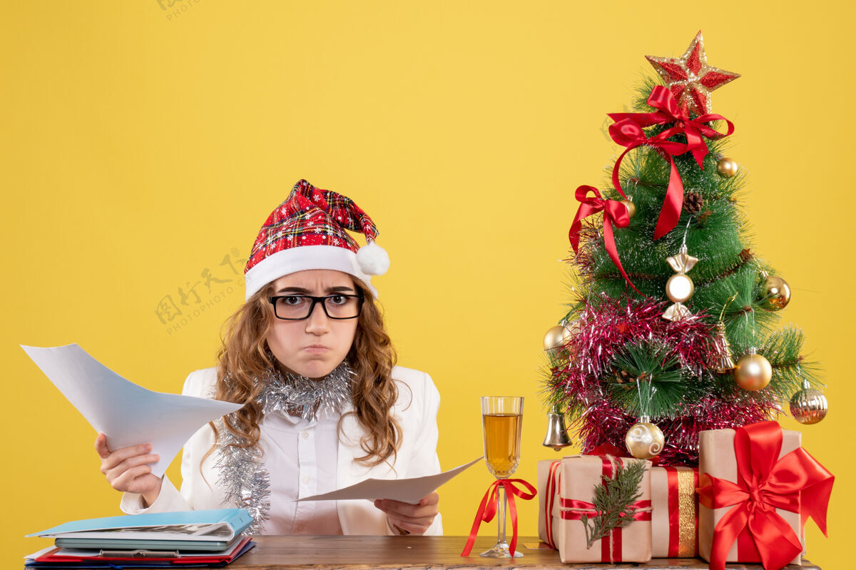 庆祝前视图女医生坐在圣诞树上 拿着黄色背景上的文件女医生健康礼物