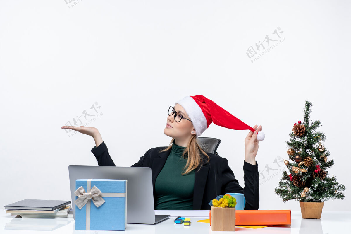 眼镜一位年轻的女士拿着圣诞树和礼物坐在桌子旁 手里拿着圣诞老人的帽子和眼镜圣诞老人玩圣诞老人