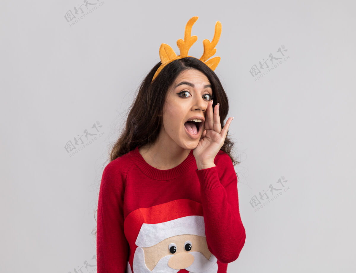毛衣印象深刻的年轻漂亮女孩穿着驯鹿鹿角头带和圣诞老人毛衣看着耳语印象深刻新年年