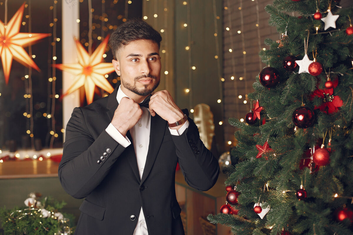 庆祝圣诞树旁的帅哥穿着黑色西装的绅士奢侈享受庆祝
