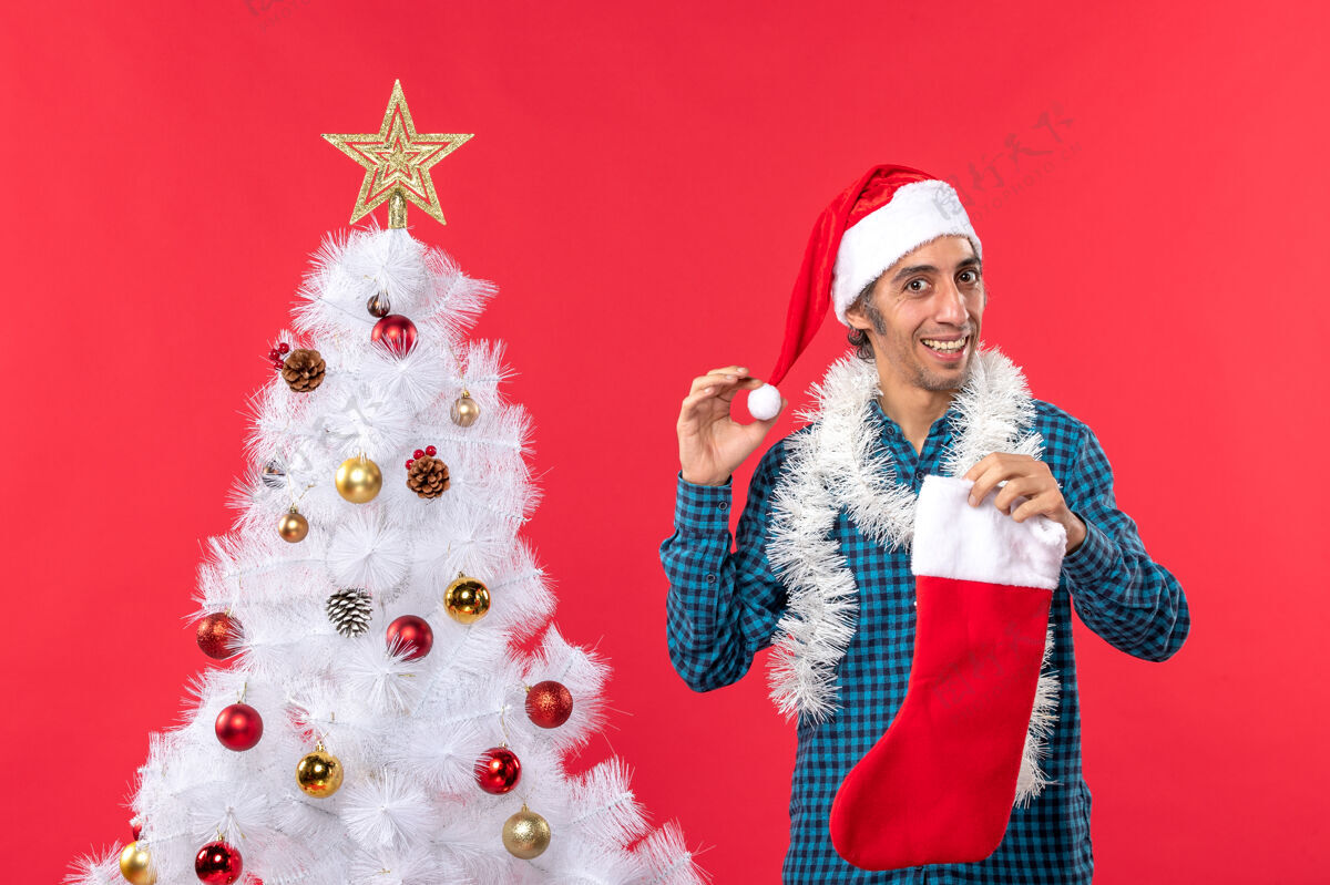 圣诞年轻人戴着圣诞老人的帽子 拿着圣诞袜子和装饰品 新年的气氛男人帽子配件