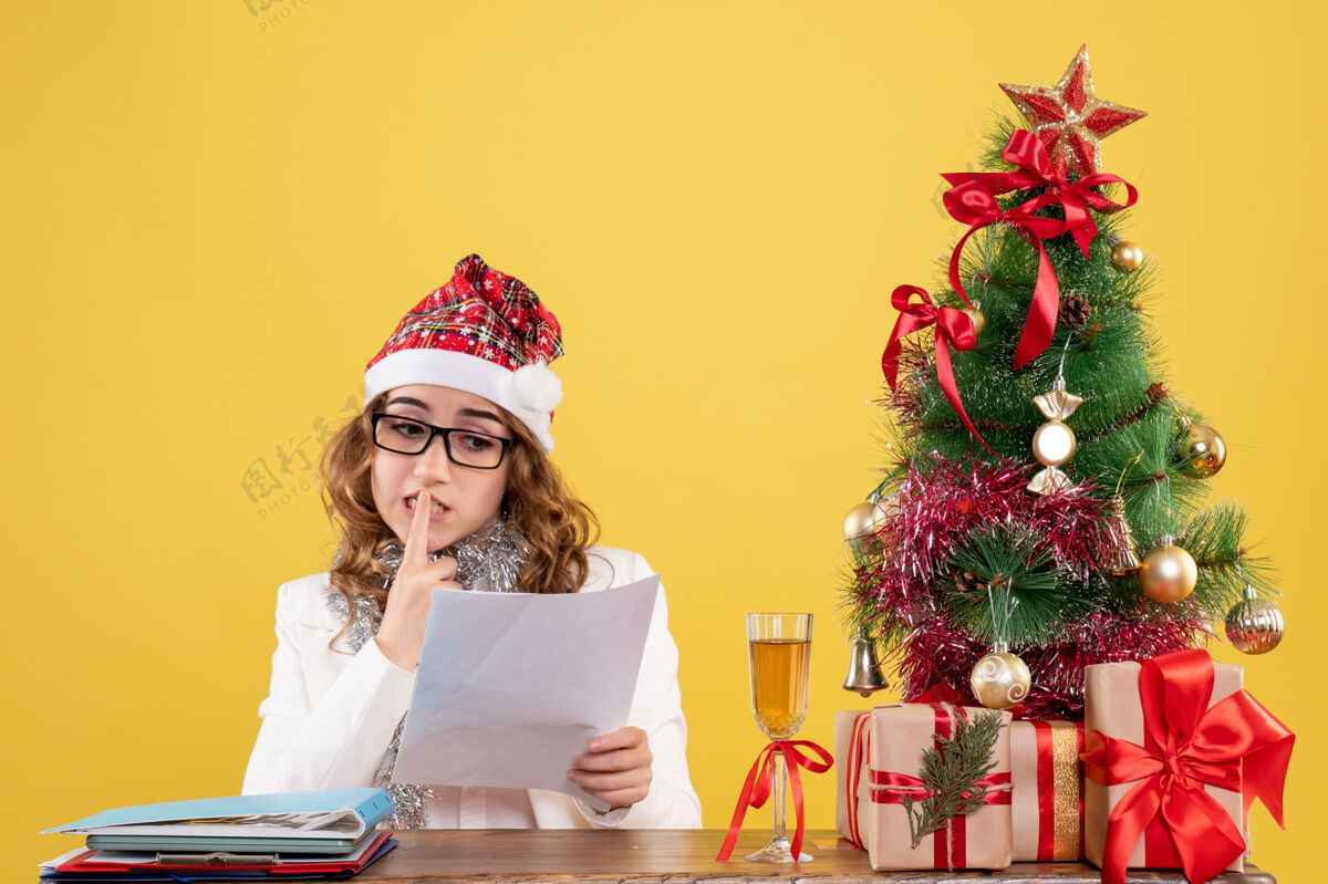 树前视图女医生坐在圣诞树上 拿着黄色背景上的文件女医生文件花