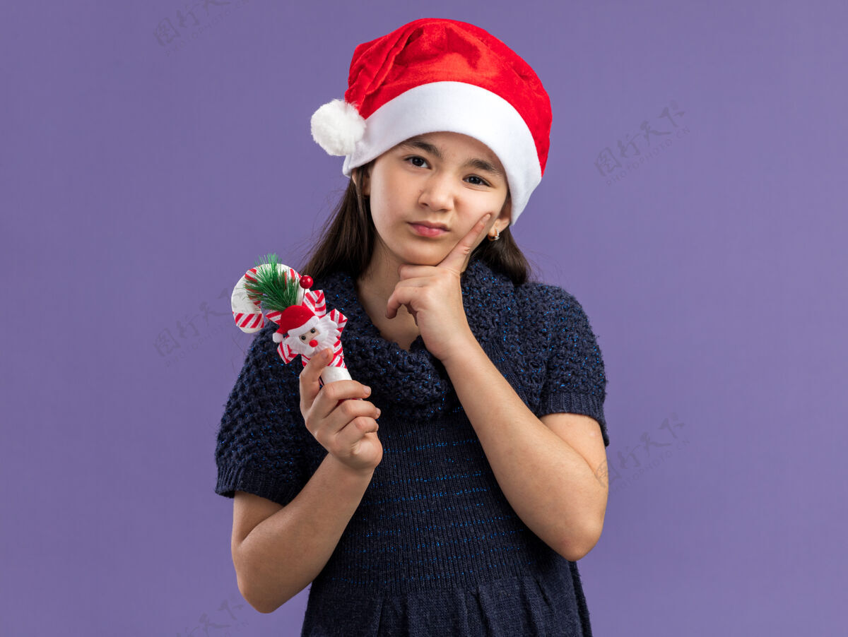 编织小女孩穿着针织连衣裙戴着圣诞帽拿着圣诞糖果手杖神情悲伤新年圣诞老人圣诞