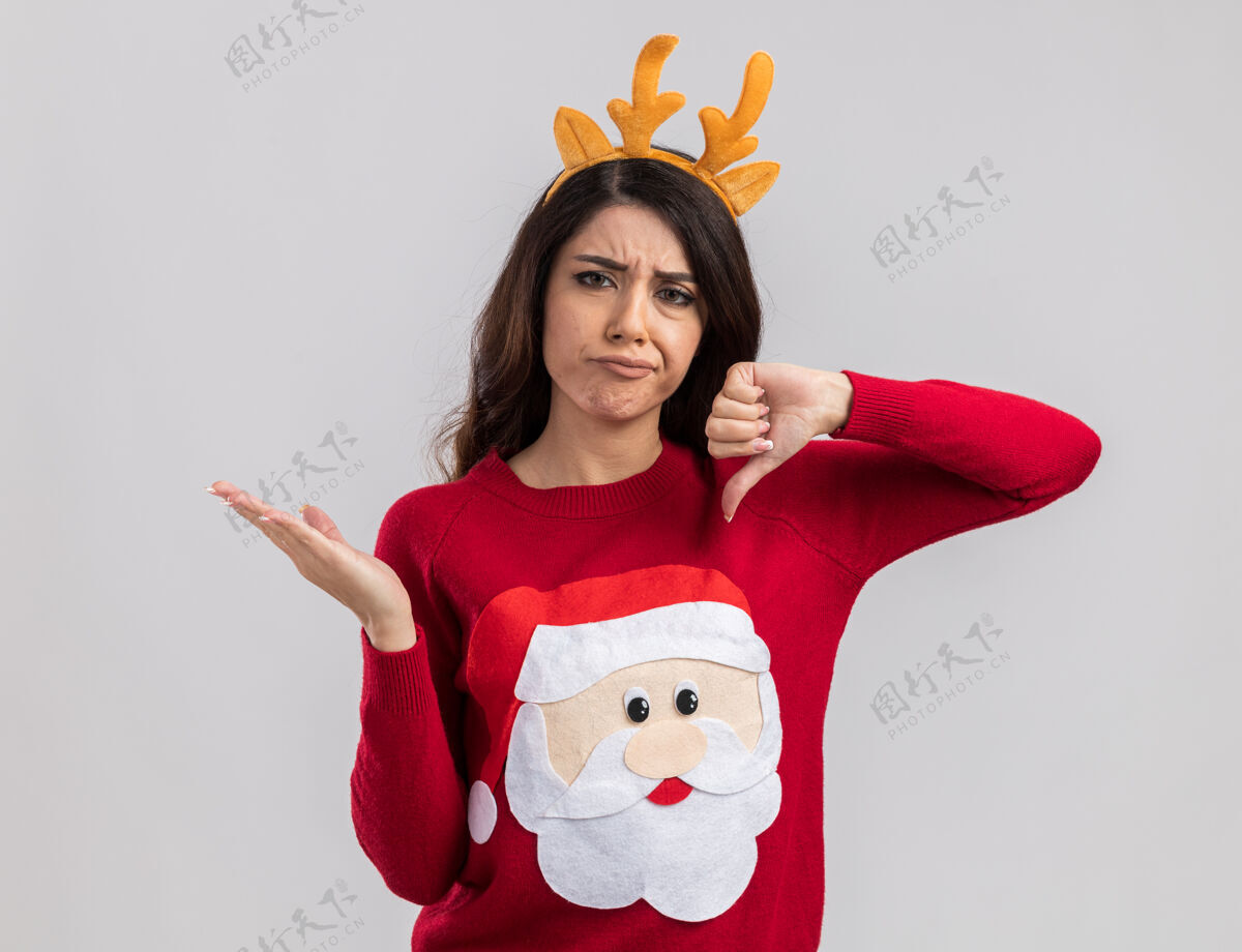 拇指穿着驯鹿鹿角头带和圣诞老人毛衣的年轻漂亮女孩看起来空手而下鹿角毛衣圣诞