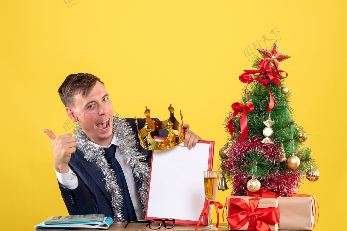 拇指商务人士在圣诞树旁的桌子旁做竖起大拇指的招牌 黄色的礼物坐着商务圣诞节