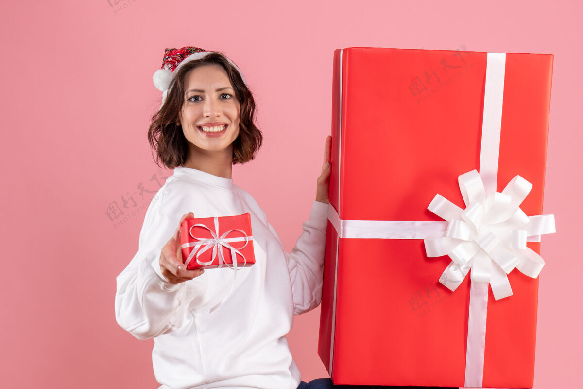 粉色年轻女子手持小圣诞礼物 粉红色墙上挂着一个大圣诞礼物情感圣诞节购物