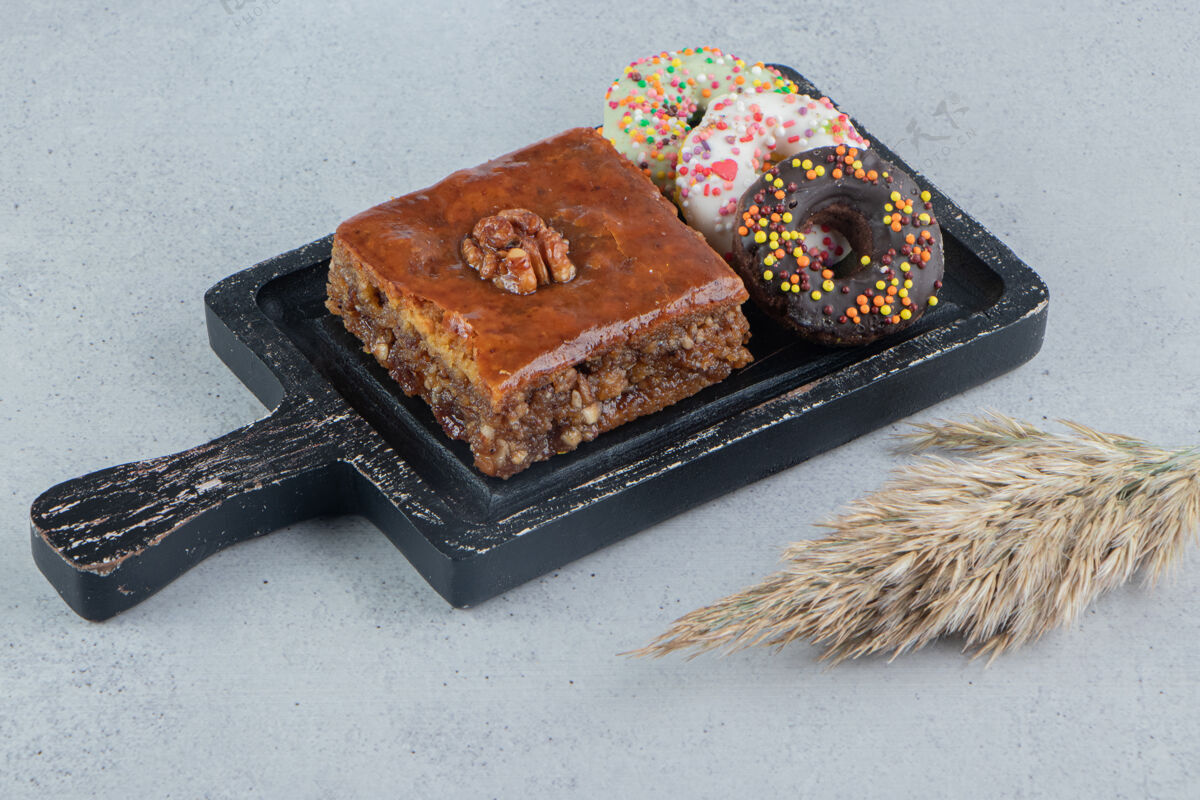 糖甜甜圈和烤面包放在一个小盘子里 旁边是大理石背景上的一根羽毛草茎烘焙美味核桃