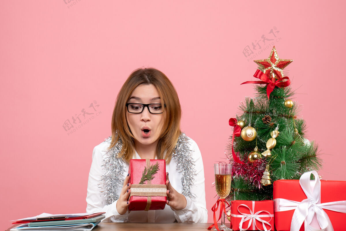 圣诞节女工人坐在粉红色的圣诞礼物和圣诞树旁的正视图礼物情感工作