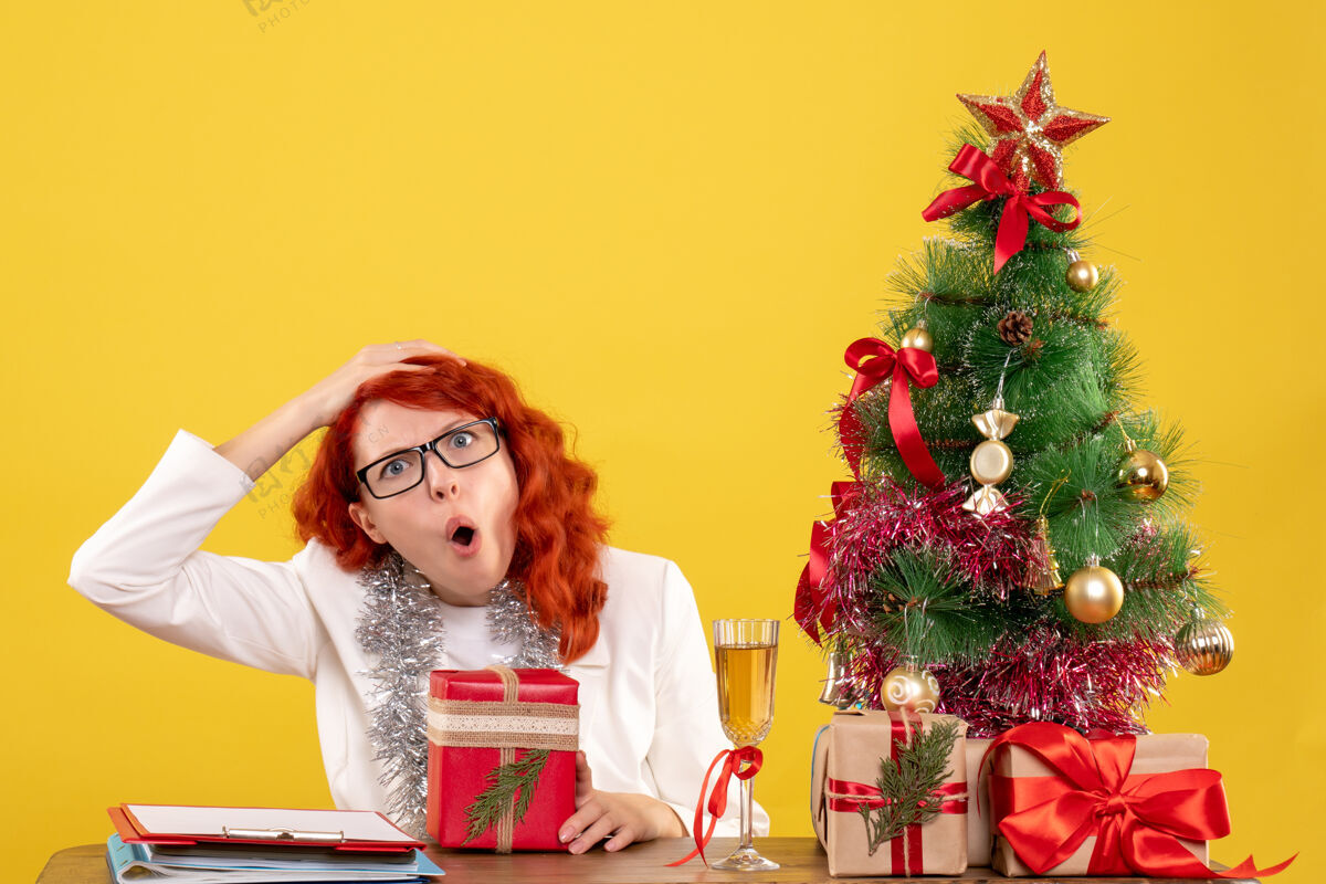 背景前视图：女医生坐在桌子后面 黄色背景上有圣诞礼物微笑圣诞节快乐