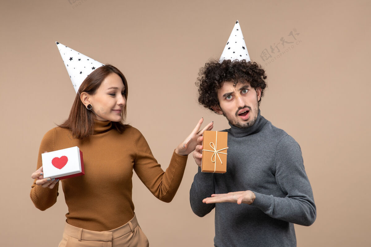 礼物新年拍摄与惊喜年轻夫妇戴新年帽女孩的心和男孩的礼物灰色年轻帽子惊讶