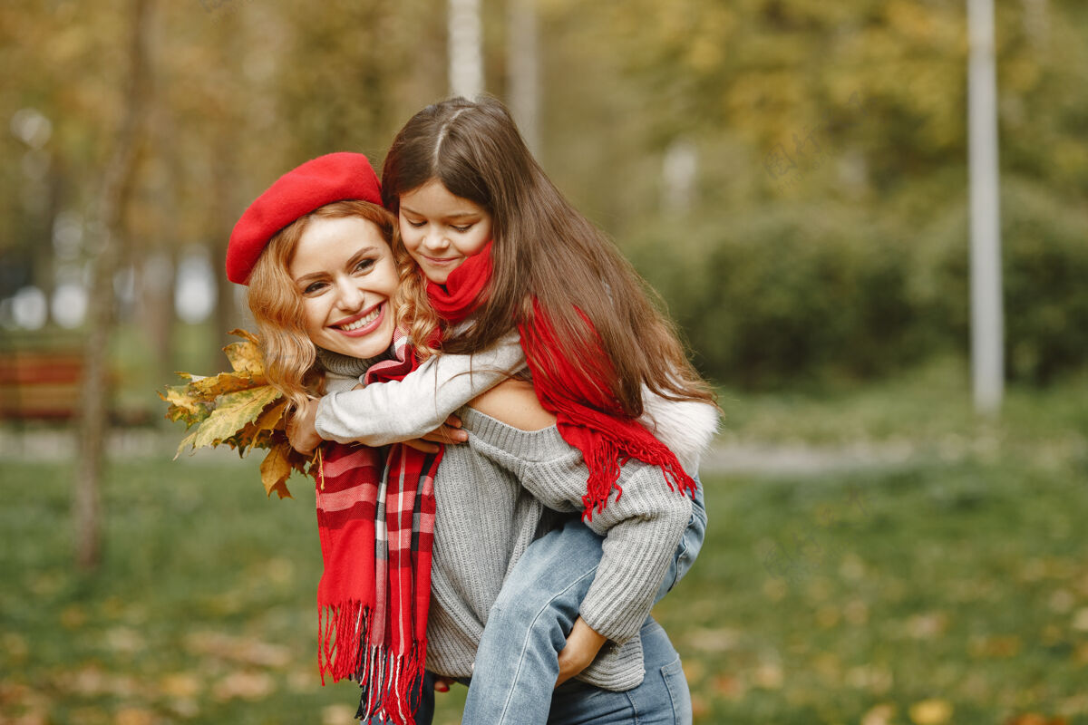 玩耍时髦的母亲带着女儿黄色的秋天戴着红领巾的女人欢乐金发叶子