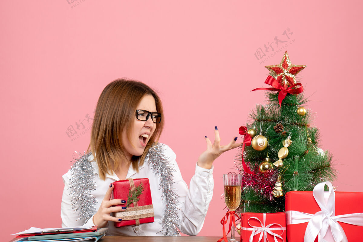 工人女工正坐在粉红色的椅子上 手里拿着圣诞礼物坐着工作情感