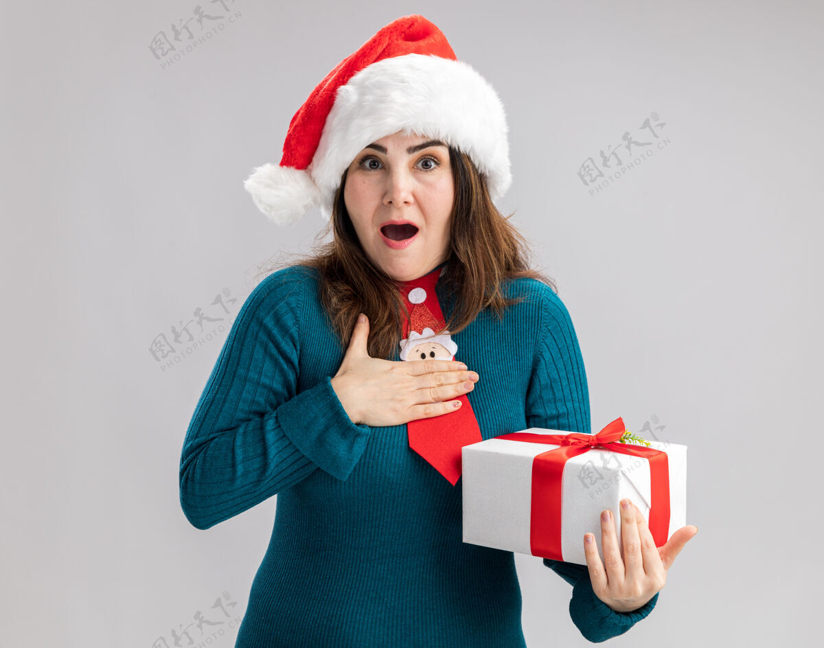 兴奋兴奋的成年白人妇女戴着圣诞帽 打着圣诞领带 把手放在胸前 拿着一个白色背景的圣诞礼盒 里面有复印空间领带帽子盒子