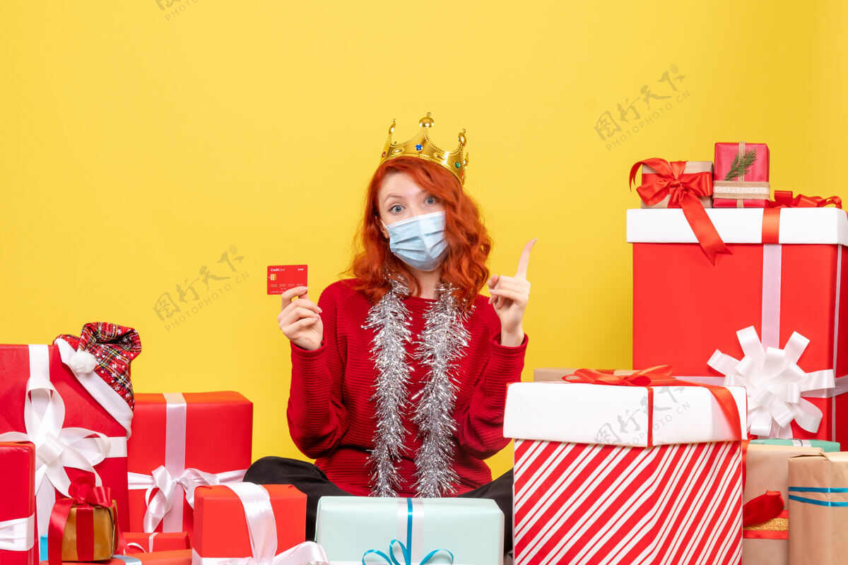 银行正面图是一位年轻女子戴着面具围坐在礼物旁边 黄色的墙上挂着银行卡年轻女性人圣诞节
