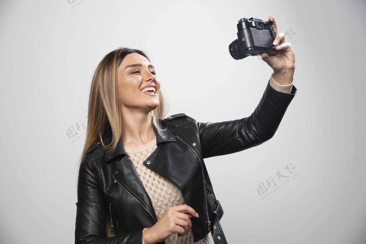 模特一位身穿黑色皮夹克的年轻女士 以积极微笑的态度用相机拍照服装乐趣数码