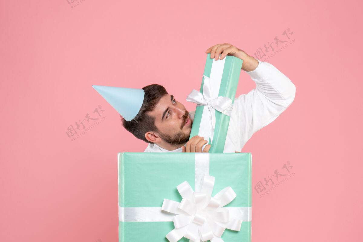 庆祝年轻人站在粉红色墙上的礼物盒里的正面图礼物粉色盒子