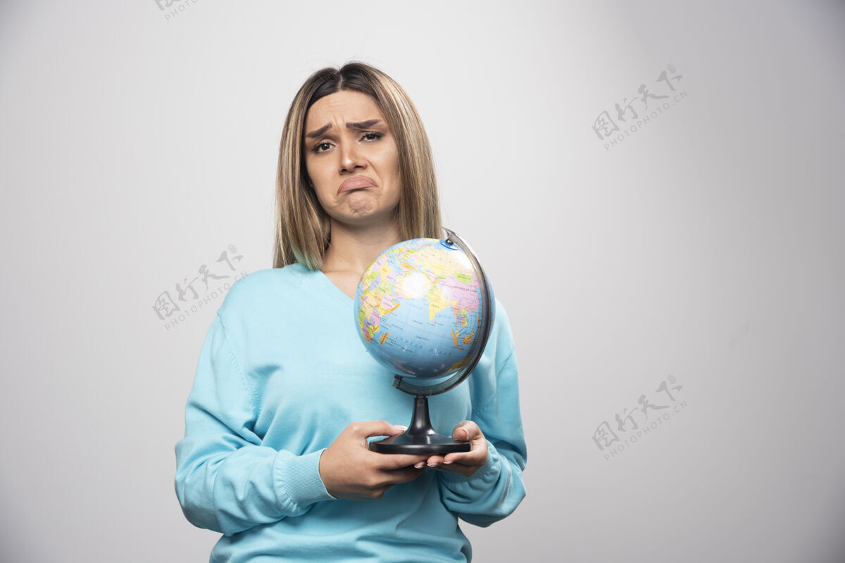 女人穿着蓝色运动衫的金发女孩手里拿着一个地球仪 看上去既不确定又困惑怀疑年轻人