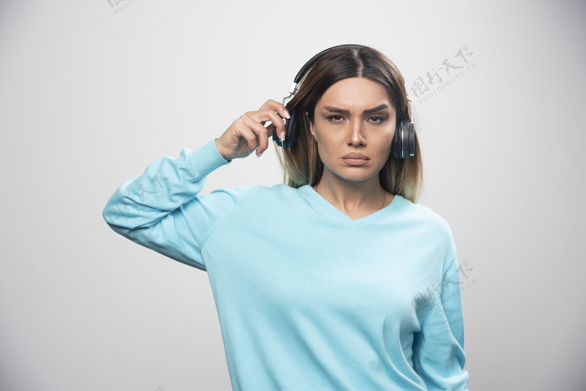 成人穿着蓝色运动衫的金发女孩戴着耳机 努力听懂音乐人专心耳机