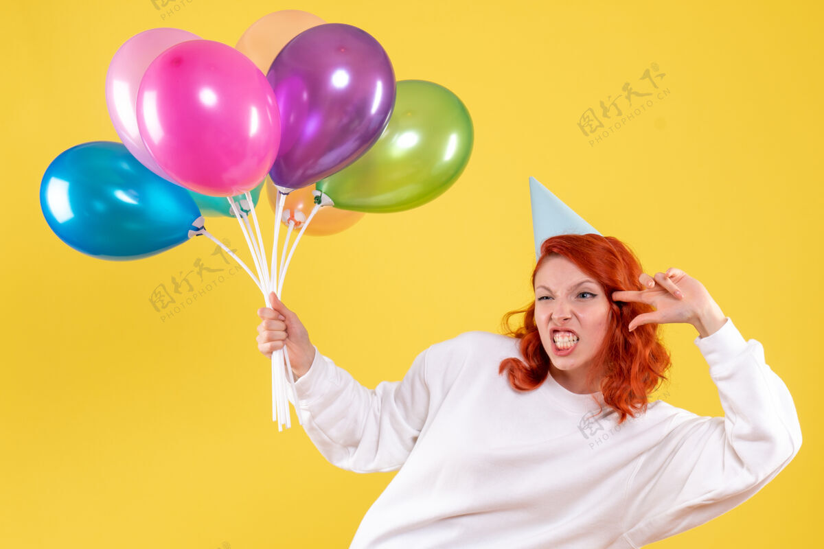 气球黄色墙壁上手持可爱彩色气球的年轻女子的正视图生日举行女人