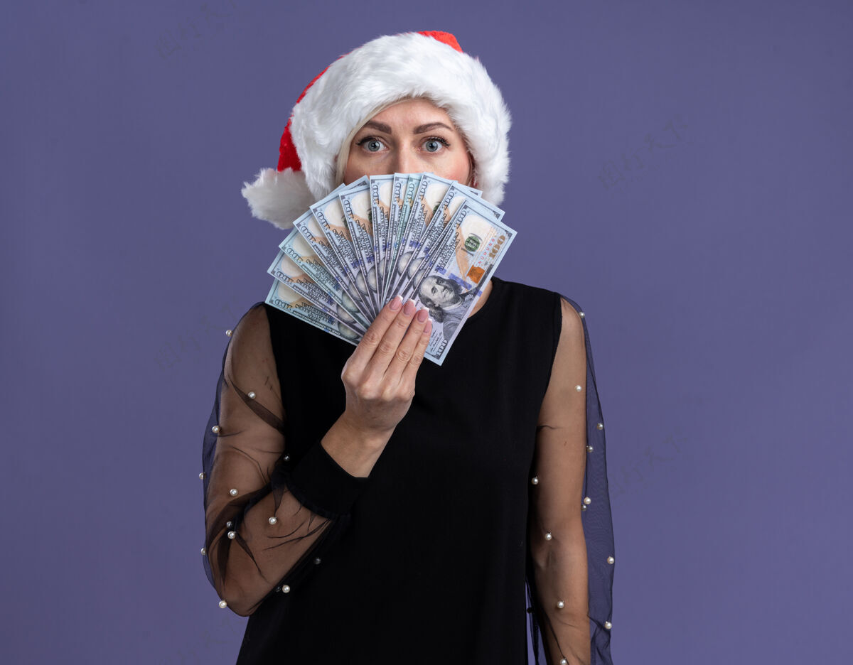 中年印象深刻的中年金发女人戴着圣诞帽拿着钱从后面隔离在紫色的墙上与复制空间帽子圣诞节穿着