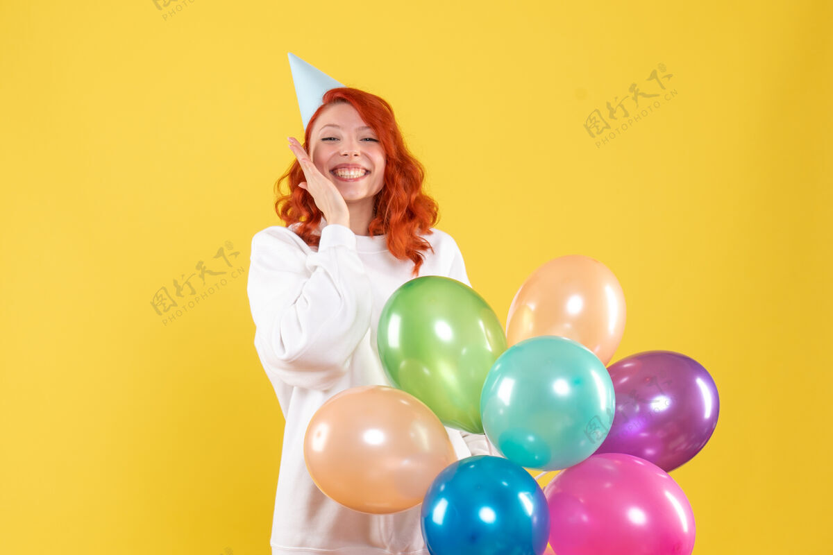 年轻的女性黄色墙壁上手持彩色气球的年轻女子的正视图气球生日庆祝