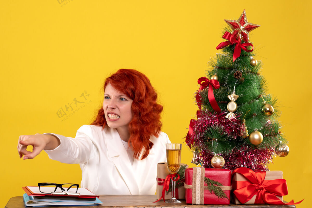 黄色女工人坐在桌子后面 手里拿着圣诞礼物和黄色的圣诞树情感安排办公室