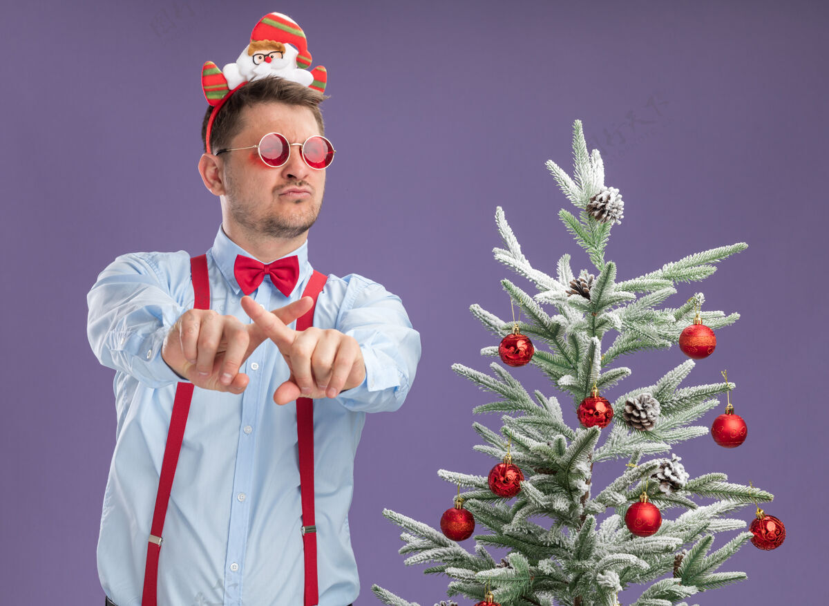 脸戴吊带领结的年轻人站在圣诞树旁 戴着圣诞老人和红眼镜新严重圣诞