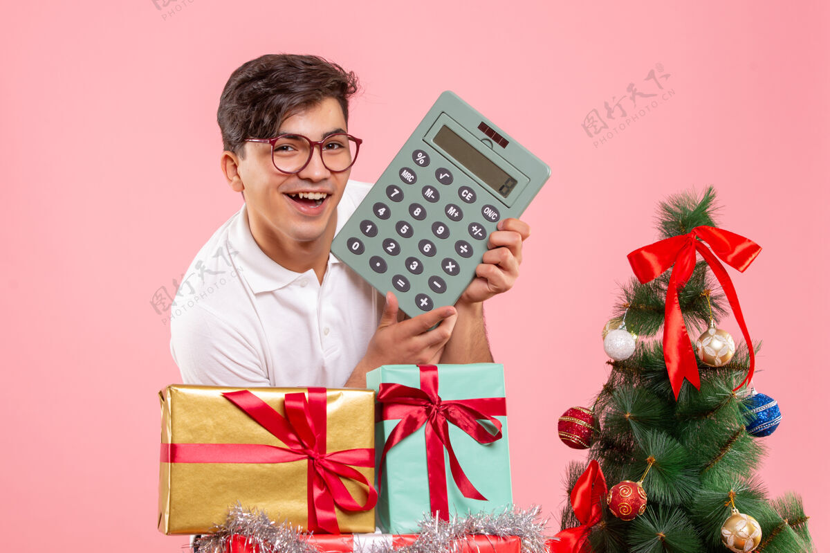 年轻男性圣诞节前后年轻人的正面图 粉色墙上有计算器商务成人快乐