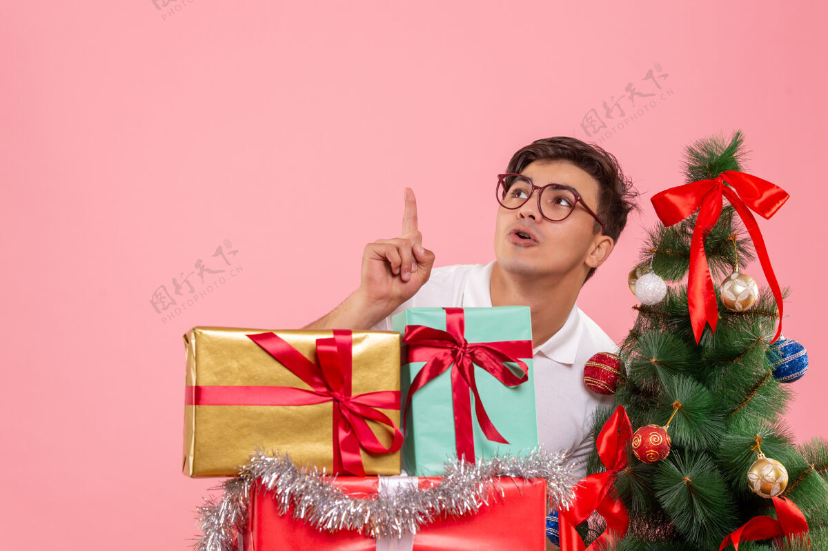 快乐年轻人在圣诞礼物和粉红色墙上的圣诞树前视图丝带快乐粉色