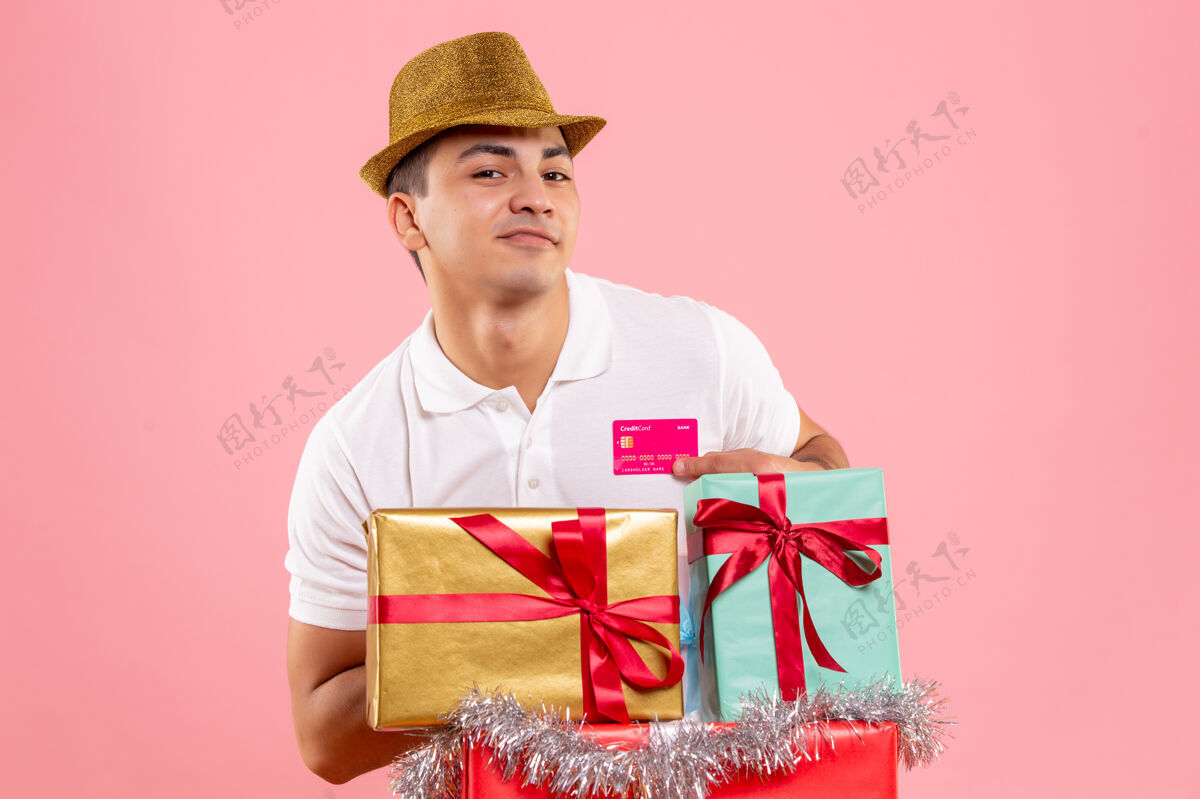 礼物年轻人在圣诞节前后的正面图 粉红色的墙上挂着一张银行卡前面十二月人们